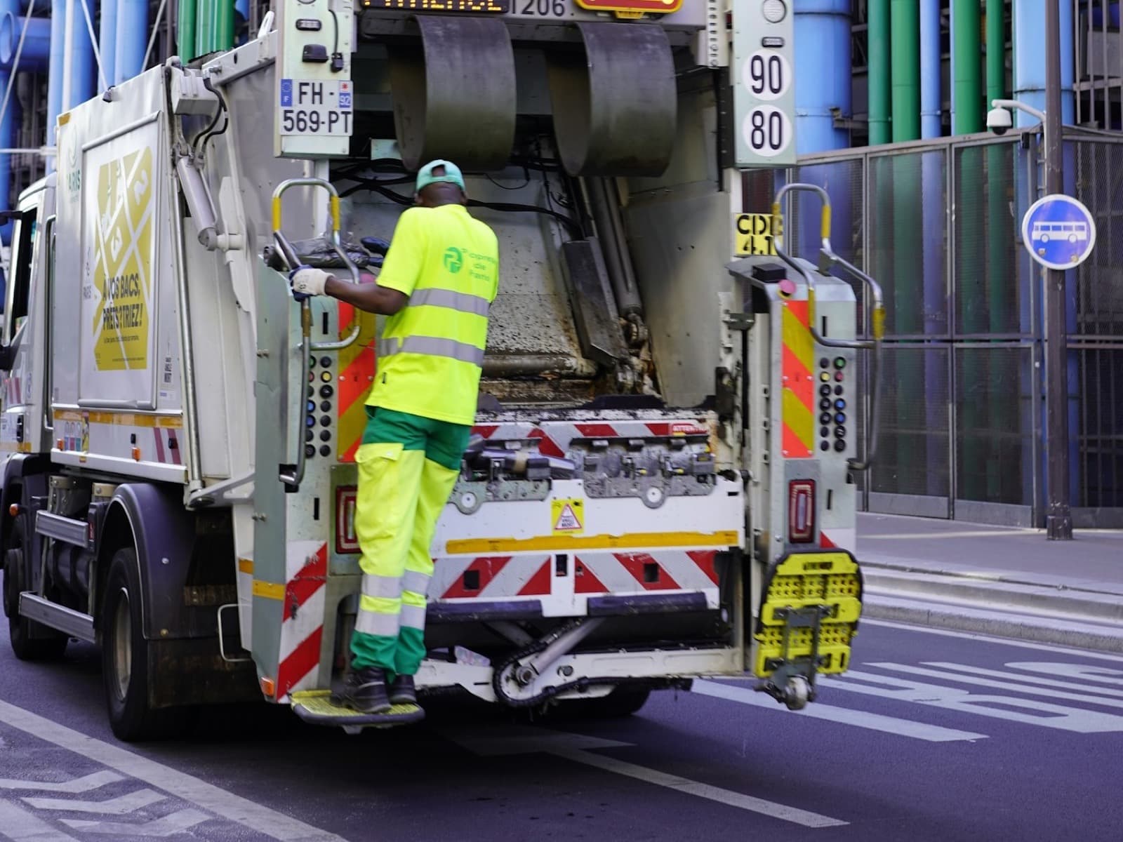 Éboueur de dos à l'arrière d'un camion de collecte, dans une rue de Paris